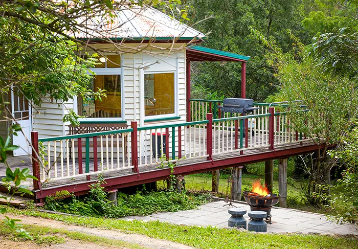 Outdoor fire pit with open fire blazing, stools for sitting around the fire outside the holiday accommodation and its balcony with BBQ.