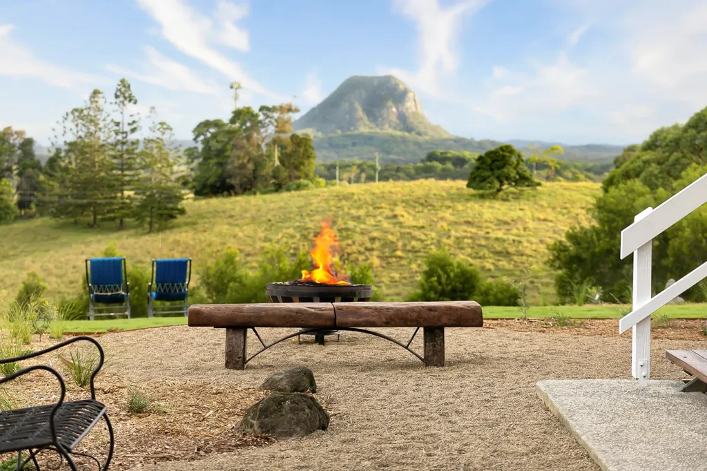 Chunky wooden bench in front of a roaring open fire pit that overlooks Mount Cooroora.